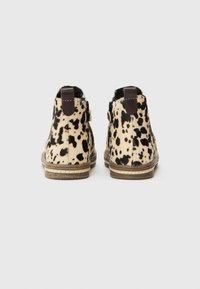 Botas de tobillo de estampado de leopardo hechas de piel con un acento de cuero marrón en el talón y una suela de goma plana. Presenta costuras decorativas.