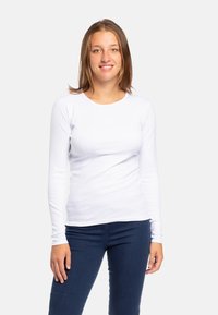 Maglietta bianca in cotone a maniche lunghe con scollo rotondo, indossata con jeans blu scuro, caratterizzata da un design aderente e una trama liscia.
