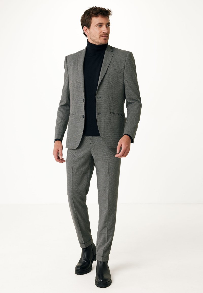 Šedý kostkovaný oblek s přiléhavým střihem, zahrnující dvoucestný blejzr a slim kalhoty, doplněný černým rolákem a černými botami.