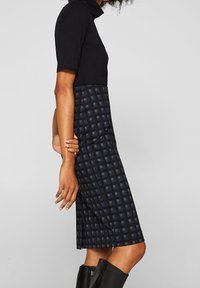 Svart kortärmad topp kombinerad med en knälång marinblå rutmönstrad kjol. Materialet verkar slätt; kjolen har en lätt svängning i botten.