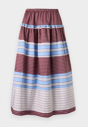 Femme portant un haut beige sans manches, une jupe longue rayée bordeaux, bleue et blanche, des sandales marron et un sac à bandoulière rouge foncé.