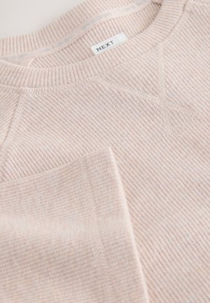 Šviesiai rožinė ribuota sportinė palaidinė su apvalia iškirpte, siuvimo detalėmis ir etikete, kurioje parašyta „NEXT“. Minkšta tekstūra su subtiliu raštu visame paviršiuje.