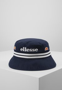 Marinblå bucket-hatt med vita randiga detaljer, broderad "ellesse"-logotyp och en liten flerfärgad logotyp. Tillverkad av lättviktig tyg.
