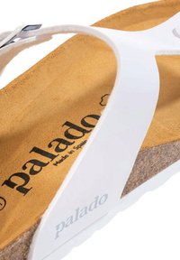 Hvid thong sandal med en korksål og en tan ruskinds indersål. Mærkenavnet "palado" er trykt i sort på sålen.