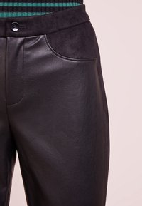 Byxor i en blandning av svart läder och mocka med sidofickor, en slät textur och knäppning i midjan.