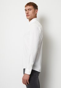 Witte blouse met lange mouwen en een button-down kraag, gemaakt van een gladde stof. Met knoopmanchetten en een getailleerde pasvorm, gecombineerd met donkerblauwe spijkerbroek.