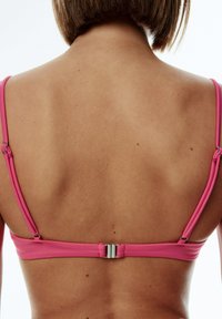 Rosa Bikini-Oberteil mit dünnen Trägern und einem silbernen Verschluss auf der Rückseite, das eine glatte Stofftextur auf gebräunter Haut zur Schau stellt.