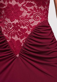 Robe rouge foncé avec corsage en dentelle florale et tissu froncé rassemblé à la taille, créant un détail en forme de V.