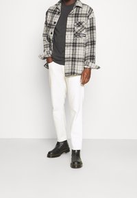 Svart och vit rutig flanellskjorta över en grå t-shirt, ihopparad med vita slim-fit byxor och svarta chelsea boots.