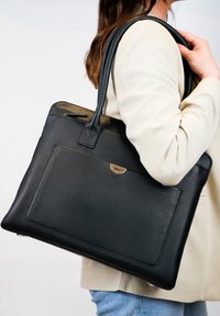 Zwarte leren tote bag met een gladde textuur, een voorkantzak en metallic hardware accent. Voorzien van twee lange handvaten voor het dragen.