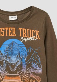 Bruine lange mouwen shirt met een dinosaurustekening in blauw en oranje en de tekst "Mister Truck CHASE!" op de voorkant.