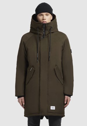 Olive green parka with a high collar, adjustable drawstrings, front zip, and side pockets. Features a logo patch on the lower front.