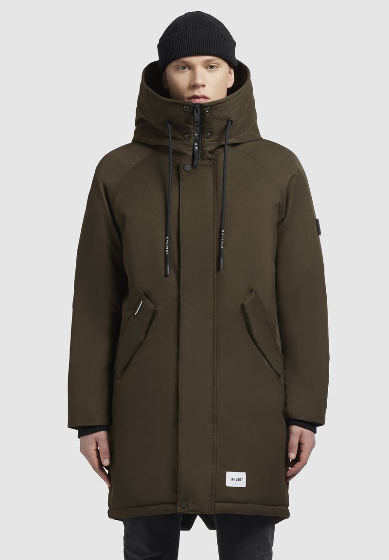 Parka verde măsliniu cu guler înalt, șnururi ajustabile, fermoar frontal și buzunare laterale. Dispune de o etichetă logo pe partea de jos din față.