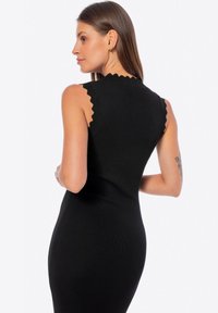 Abito nero a costine con bordi a scallop sulle spalle, silhouette aderente e lunghezza media. Tessuto liscio con un design snello.