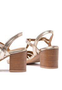 Sandalias de tacón metálico dorado con diseño de tiras y un tacón de bloque de madera, que presentan una superficie texturada y puntera abierta para mayor transpirabilidad.