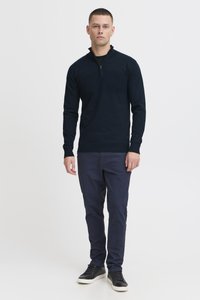 Sudadera de media cremallera en color azul marino, hecha de tejido de punto, combinada con pantalones azul oscuro y zapatillas negras. Diseño simple con mangas largas y dobladillo acanalado.