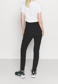 Pantalones deportivos negros con un diseño entallado, cintura elástica y acentos en contraste. Combinados con una camiseta blanca de manga corta.