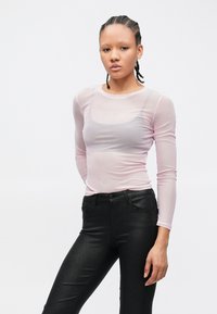 Haut en mesh rose clair à manches longues, associé à un jean noir ajusté et brillant. Le haut présente un col rond et une texture transparente.