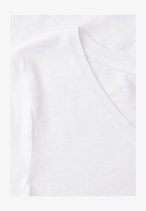 Dettaglio ravvicinato del tessuto e delle cuciture di una maglietta bianca in cotone con scollo a V, che mette in risalto la trama e le linee delle cuciture.