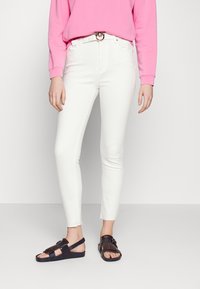 White skinny jeans with a frayed hem, paired with a bright pink sweatshirt and brown/black sandals featuring a fringe design.