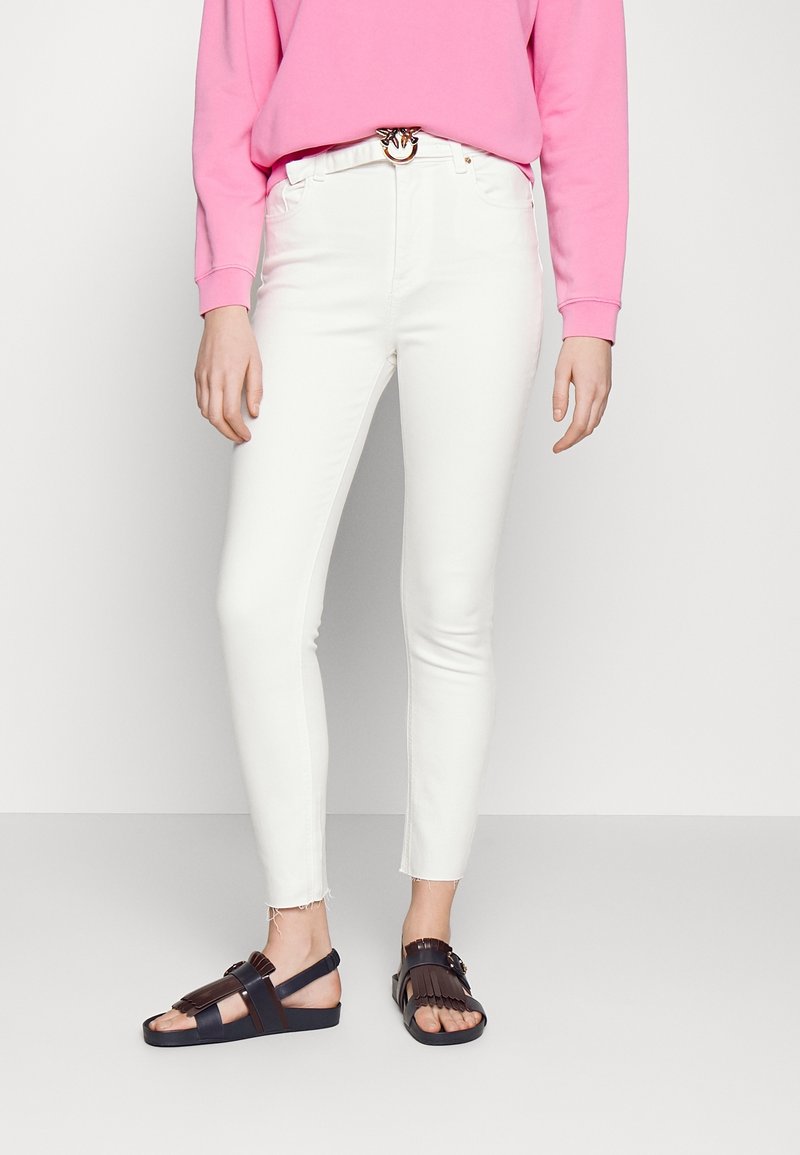 White skinny jeans with a frayed hem, paired with a bright pink sweatshirt and brown/black sandals featuring a fringe design.