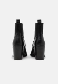 Bottes cheville en cuir noir avec un talon carré haut, panneaux latéraux élastiques et languette à l'arrière. Finition lisse avec un minimum de détails.