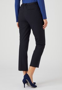 Zwart gestreepte, op maat gemaakte broek van stof met een gladde textuur, met een halflange taille en een cropped lengte, gecombineerd met marineblauwe hakken.