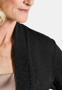 Zwarte cardigan van een zachte, textuurstof met een subtiele glans. De kraag heeft een gedrapeerd ontwerp dat het schoudergebied accentueert.