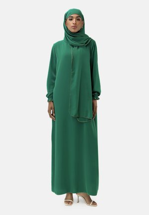 Vestido de noche verde con mangas largas y un hijab a juego. Tejido fluido, adornado con finos acentos dorados y un corte relajado.