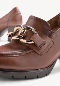 Mocassini in pelle marrone con un accento in catena d'oro, con tacco basso a blocco e cuciture dettagliate lungo il bordo. Texture liscia, design classico.