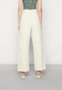 Brede, crèmekleurige broek met een hoge taille, met een soepele textuur en twee achterzakken. Draagt men met lichte platform sandalen.