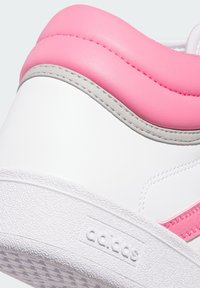Primo piano del tallone di una sneakers Adidas bianca con colletto imbottito rosa e logo del brand in rilievo sulla suola testurizzata.