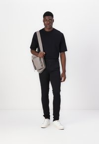 Black short-sleeve t-shirt, black slim-fit pants, white sneakers, and a light gray crossbody bag with two front pockets, on a plain background.