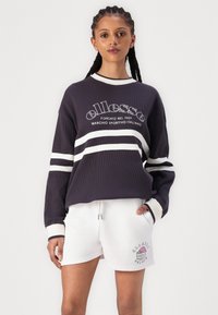 Sudadera de canalé azul marino con rayas blancas y logo; combinada con pantalones cortos blancos que presentan un gráfico de helado impreso. Ajuste estándar y diseño casual.