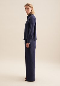 Ensemble en lin bleu marine comprenant une chemise à boutons à manches longues et un pantalon large, mettant en avant une finition texturée et des lignes épurées.