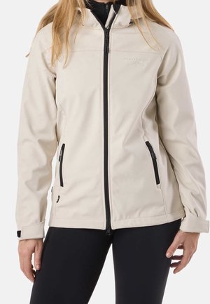 Femme portant une veste zippée beige clair avec deux poches zippées et un pantalon noir, vue des épaules aux hanches.