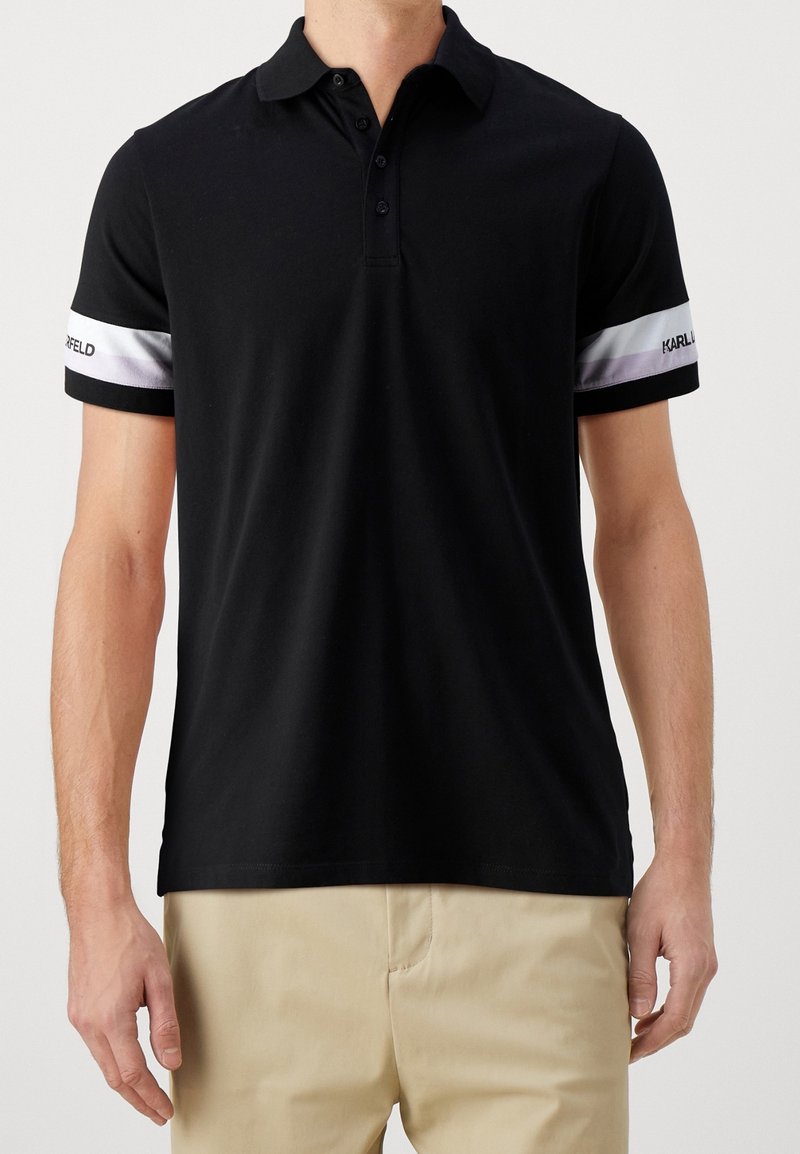 Polo shirt noir en coton. Doté d'un col classique, d'une patte de boutonnage à trois boutons et de manches rayées contrastées avec accents de logo.
