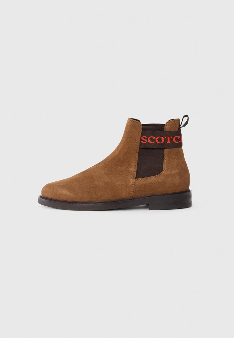 Bruine suedinen Chelsea-boot met elastische zijkanten en een zwarte band met het woord "SCOTCH" in het rood. Platte zool en afgeronde neus.