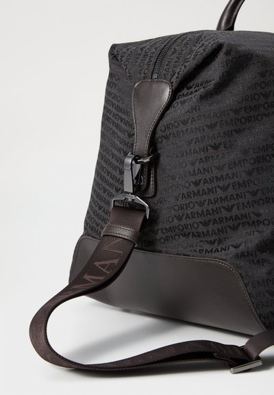 Sac en tissu noir avec un motif de logo répété, fond sombre uni, accents en cuir lisse, sangle réglable et fermeture éclair.