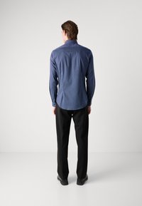 Vedere din spate a unei cămăși cu butoni, cu dungi verticale de culoare albastru închis, cu un croi ajustat și mâneci lungi, asortată cu pantaloni negri.
