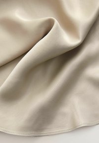 Tissu beige drapé en douces plis, présentant une texture lisse et un subtil éclat. Le bord a un détail de ourlet cousu.