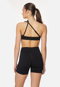 Črn športni modrček s prečnimi naramnicami, v kombinaciji s črnimi kratkimi hlačami visoke pasu. Gladka tekstura, prilegajoč dizajn, brez vidnih vzorcev ali dodatkov.