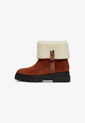 Brown suede ankle boot with a white faux fur cuff. Features a sturdy black rubber sole and a brown leather strap on the back.