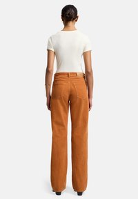 Roestkleurige corduroy wijde broek met opvallende verticale strepen, achterzakken en een aansluitende taille, gecombineerd met een witte top.