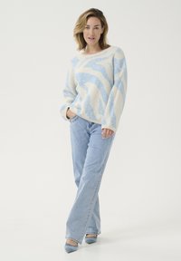 Rompertje in crème met blauw golfpatroon, ruime snit, geribbelde manchetten. Gepaard met lichtblauwe jeans en bijpassende puntenhakken.