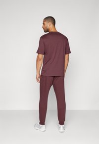 Bordo loungewear komplekts, kas sastāv no īsām piedurknēm un apaļā kakla krekla, kā arī atbilstošām biksēm ar piegrieztiem potīšu galiem, apvienots ar baltām sporta kedām.
