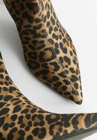 Botas de tacón alto con estampado de leopardo, punta afilada, upper de tela, en una combinación de colores negro y marrón claro, con detalles de costura sutiles.