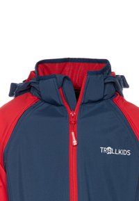 Navy and red jacket featuring a high collar, front zipper, and adjustable hood. Material appears smooth with a waterproof finish. Logo displayed.