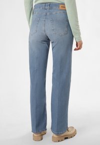 Jean en denim bleu clair avec une coupe droite et des poches arrière. Comprend une étiquette de marque brune sur la ceinture. Texture lisse.