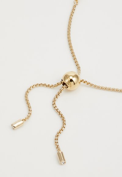 Collier en chaîne dorée mettant en vedette une perle sphérique centrale avec deux chaînes fines se terminant par des accents cylindriques, le tout avec une finition polie.